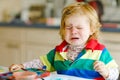 Sad crying baby girl learning painting with water colors. Little toddler child drawing at home, using colorful brushes Royalty Free Stock Photo