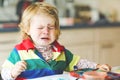 Sad crying baby girl learning painting with water colors. Little toddler child drawing at home, using colorful brushes Royalty Free Stock Photo