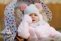 Sad crying hungry baby girl sitting in the pram or stroller on cold autumn, winter or spring day. Weeping child in warm Royalty Free Stock Photo