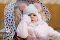 Sad crying hungry baby girl sitting in the pram or stroller on cold autumn, winter or spring day. Weeping child in warm Royalty Free Stock Photo