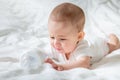 Sad and crying Infant baby girl lying on the white bed with special bottle of water with nipple. Tries to gnaw her. teething Royalty Free Stock Photo