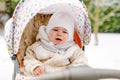 Sad crying little baby girl sitting in the pram or stroller on winter day. Unhappy upset tired and exhausted child in Royalty Free Stock Photo