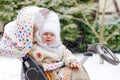 Sad crying little baby girl sitting in the pram or stroller on winter day. Unhappy upset tired and exhausted child in