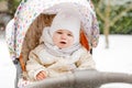 Sad crying little baby girl sitting in the pram or stroller on winter day. Unhappy upset tired and exhausted child in Royalty Free Stock Photo