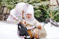 Sad crying little baby girl sitting in the pram or stroller on winter day. Unhappy upset tired and exhausted child in