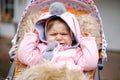 Sad crying little beautiful baby girl sitting in the pram or stroller on autumn day. Unhappy tired and exhausted child Royalty Free Stock Photo