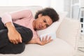 Sad crying millennial african american woman read bad message on phone, lie on sofa, suffers from pain