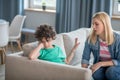 Sad curly boy sitting on sofa, blonde female talking to him, trying to cheer him up