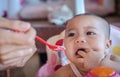 Sad cute baby refusing to eat baby food with a red spoon on a baby chai Royalty Free Stock Photo