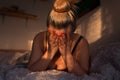 Sad, depressed blonde woman lying alone in bed, face covered with hands, with morning light