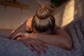 Sad, depressed blonde woman lying alone in bed, face covered with hands, with morning light