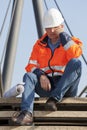 Sad or depressed engineer or foreman with protective workwear sitting in front of an industrial construction
