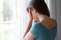 Sad depressed girl crying near the window at home in a rainy day, focus on model hand, indoor picture Royalty Free Stock Photo