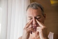 Sad and depressed man holding his head with his hand, standing by the window.