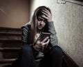 Sad depressed unhappy teenager girl suffering from cyberbullying by mobile smart phone sitting alone Royalty Free Stock Photo