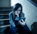 Sad depressed unhappy teenager girl suffering from cyberbullying by mobile smart phone sitting alone Royalty Free Stock Photo