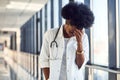 Sad and depressed young african american female doctor in white uniform standing in corridor Royalty Free Stock Photo