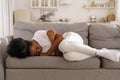 Depressed Black girl with crossed arms lying on couch at home crying, suffering from breakup.