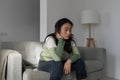 Sad depressive Korean woman sitting on sofa thinking about failure, having psychological problems