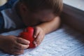 Sad and desperate child boy holding red toy heart in hands and hiding his face