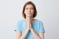 Portrait of sad desperate young woman in blue t shirt keeps hands in praying position and asking for help isolated over white Royalty Free Stock Photo