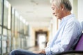 Sad and devastated asian old man sitting in hospital hallway