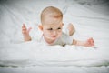 Sad and disappointed baby girl in white clothes is lying on a white bed and looking at right, Infant child  lying on her stomach Royalty Free Stock Photo