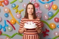 Sad disappointed woman with brown hair wearing striped dress holding cake she dislikes mixing order buying wrong dessert standing