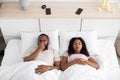 Sad disgruntled millennial african american husband closes nose from bad scent, wife sleeps on white bed together