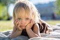 Sad displeased little child girl with blue eyes looking at camera, lying on plaid on grass, outdoor. Royalty Free Stock Photo