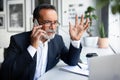 Sad dissatisfied european senior businessman in suit, glasses with laptop calls on smartphone at table