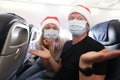 Sad and drunk man and woman in protective medical masks and santa claus red caps flying in airplane Royalty Free Stock Photo