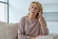 A sad elderly woman is talking on a mobile phone at home sitting on the couch Royalty Free Stock Photo