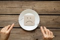 A sad emoticon lies in a plate on the table in the kitchen and next to a knife with a fork in the hands of the girls, a bad mood, Royalty Free Stock Photo