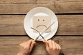 A sad emoticon lies in a plate on the table in the kitchen and next to a knife with a fork in the hands of the girls, a bad mood, Royalty Free Stock Photo