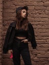 Sad emotional young woman looking unhappy near the red brick wall on the street background in black style clothing and cool cap. Royalty Free Stock Photo