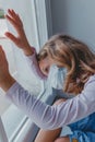 A sad European girl looks out the window with a coronovirus mask on her face. quarantine in Europe. stay home covid Royalty Free Stock Photo