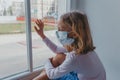 A sad European girl looks out the window with a coronovirus mask on her face. quarantine in Europe. stay home covid Royalty Free Stock Photo