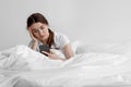 Sad european young woman suffering from depression and read message on smartphone sit on white bed at home Royalty Free Stock Photo