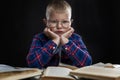 A sad fat boy with glasses sits with books at the table. Black background. Education and knowledge. Close-up Royalty Free Stock Photo