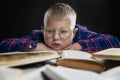 A sad fat boy with glasses sits with books at the table. Black background. Education and knowledge. Close-up Royalty Free Stock Photo