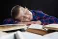 A sad fat boy with glasses sleeps at a table with books. Black background. Education and knowledge. Close-up