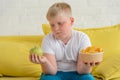 Sad fat boy looking at an apple and holding a cup of chips in another hand