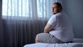 Sad fat man sitting on bed at home, looking at camera, depression, insecurities Royalty Free Stock Photo