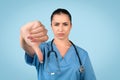 Sad female nurse with thumbs down on blue background Royalty Free Stock Photo