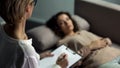 Sad female patient lying on sofa and talking with psychologist, therapy session