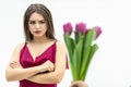 Sad frowning young woman standing with arms crossed and looks displeaased at the tulips man gives her over white Royalty Free Stock Photo