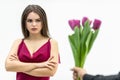 Sad frowning young woman standing with arms crossed and looks displeaased at the tulips man gives her over white Royalty Free Stock Photo