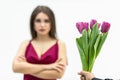 Sad frowning young woman standing with arms crossed and looks displeaased at the tulips man gives her over white Royalty Free Stock Photo