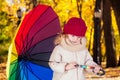 Sad funny beautiful blonde child with rainbow colorful umbrella in a gray jacket in the autumn park. Girl kid playing on Royalty Free Stock Photo